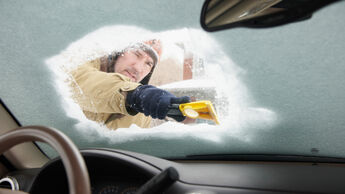 Caucasian man scraping snow off car windshield
