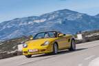 Gelber Porsche Boxster 986 Cabrio fährt auf einer kurvigen Bergstraße, im Hintergrund Gebirge, Fahrer am Steuer.