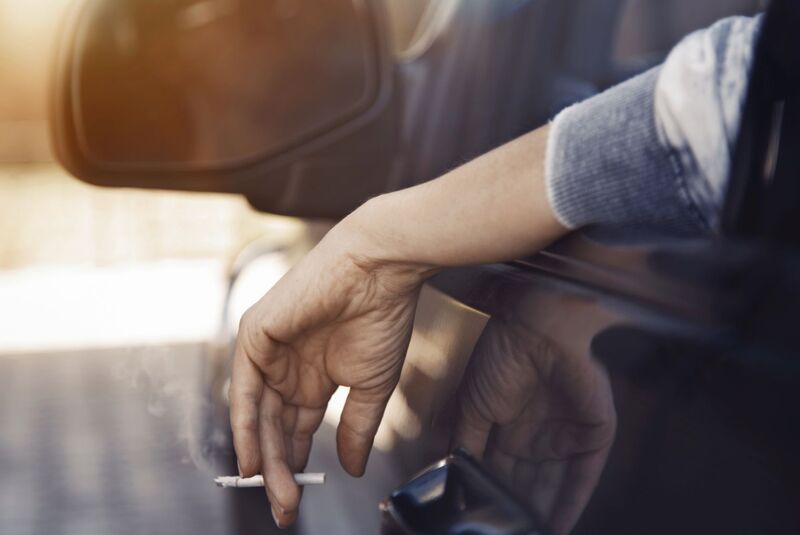 Hand of female driver in the car holding cigarette